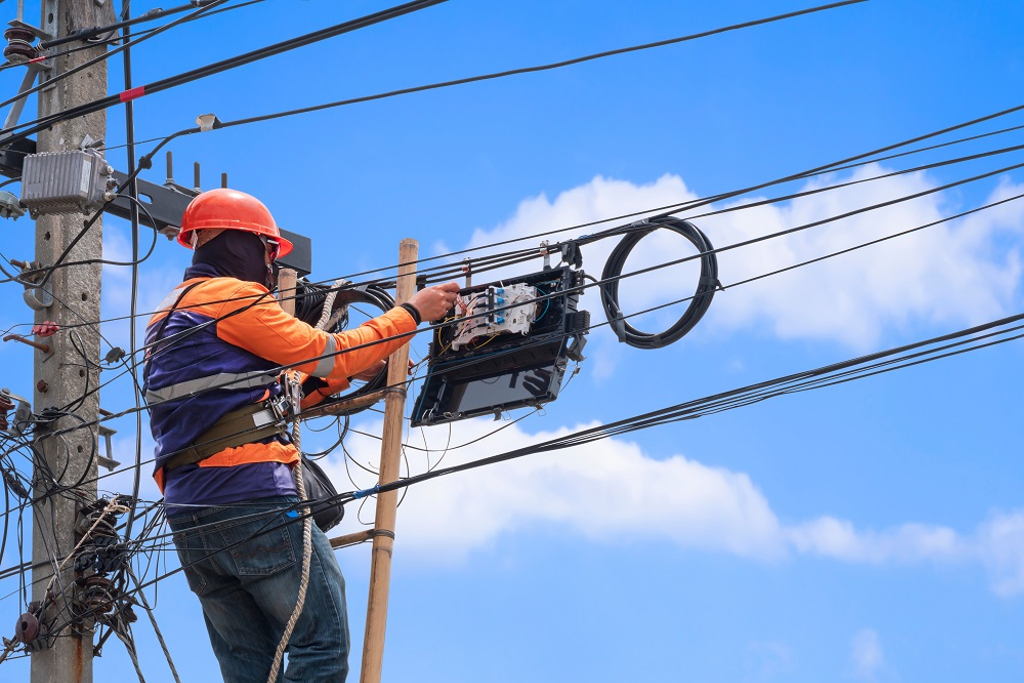 Line worker makes adjustments under a blue sky